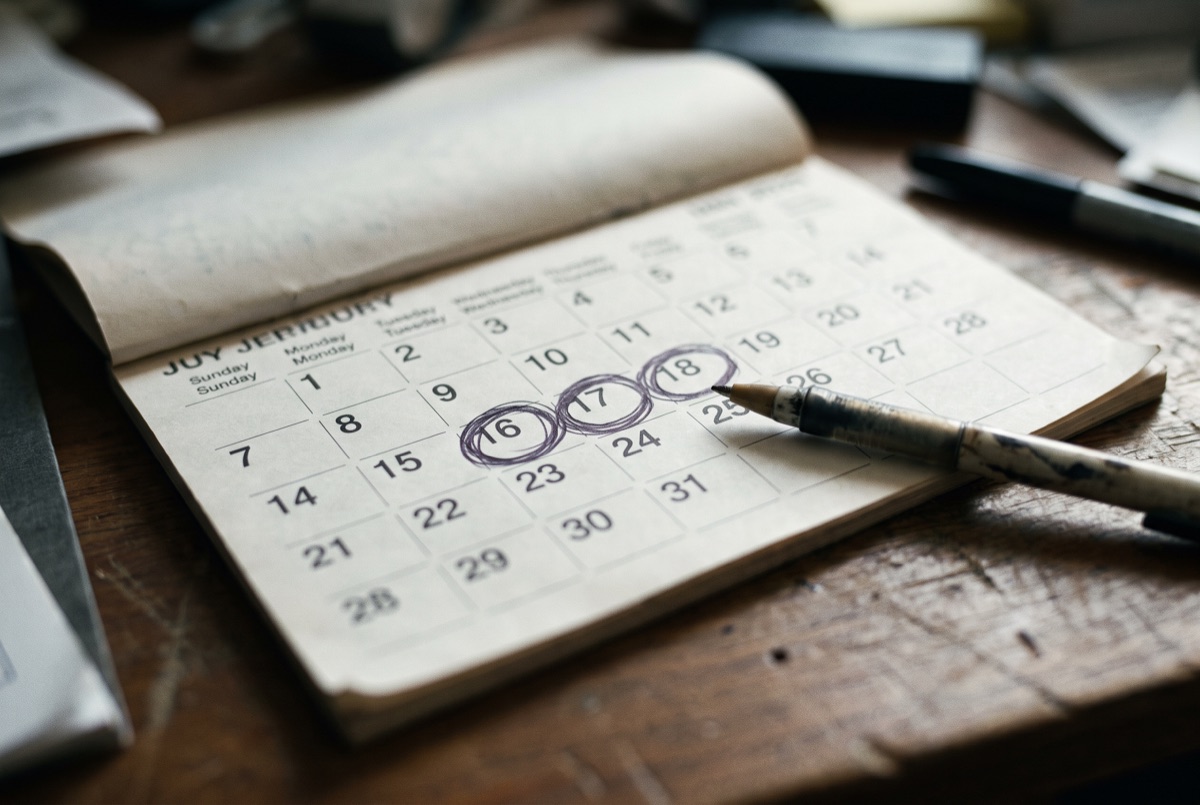 A desk calendar with dates circled, pen resting beside it