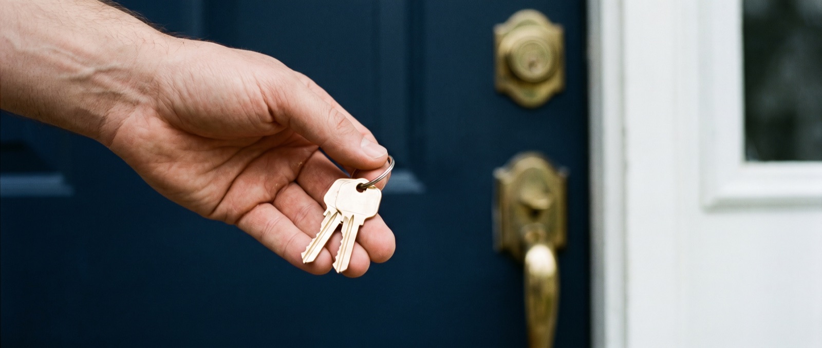 A hand holding new house keys near the front door of a modest new-construction home