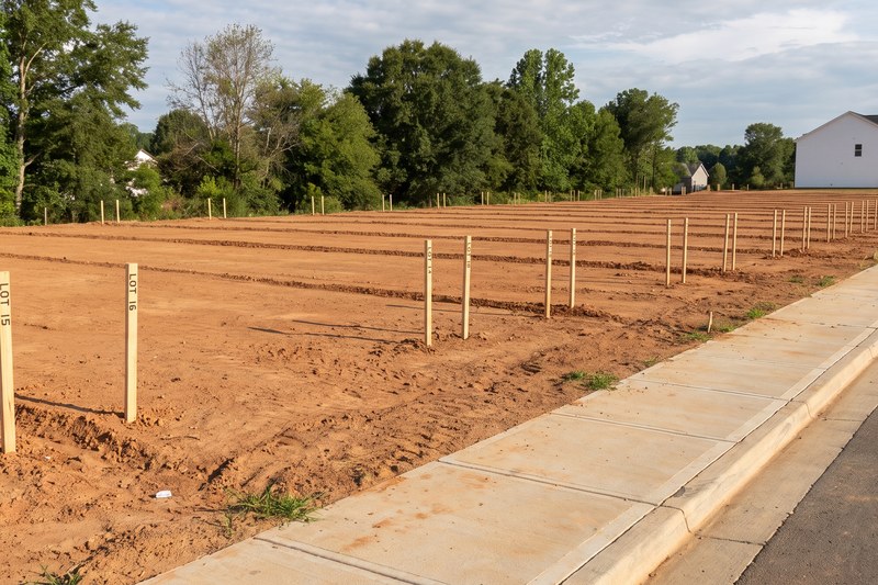 A vacant new-construction lot with surveyor stakes and a compass overlay