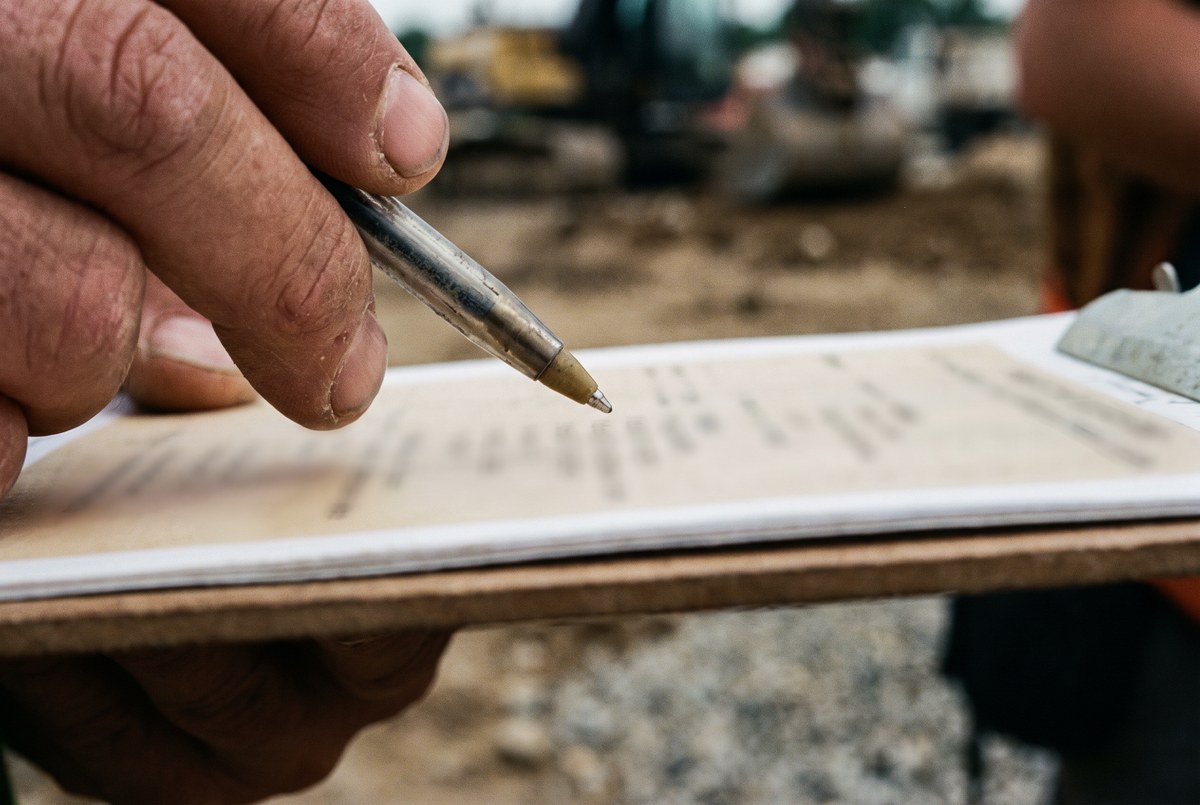A hand holding a lot grading plan document over a vacant construction lot