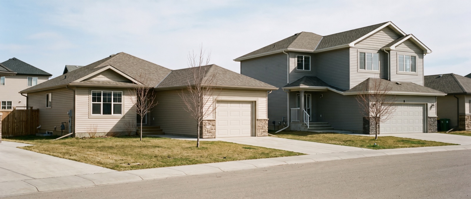 Two modest new-construction homes of different sizes side by side on a suburban street