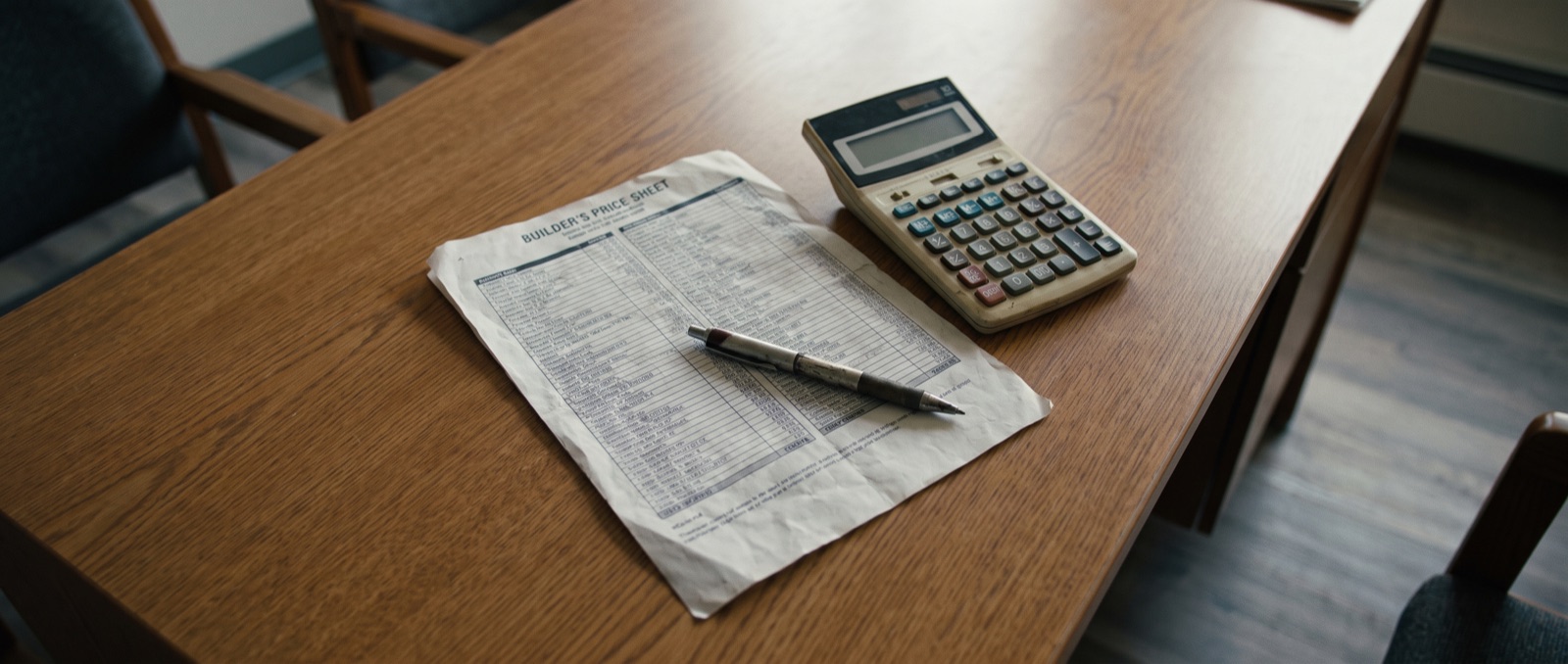 A calculator, pen, and builder price sheet on a kitchen table