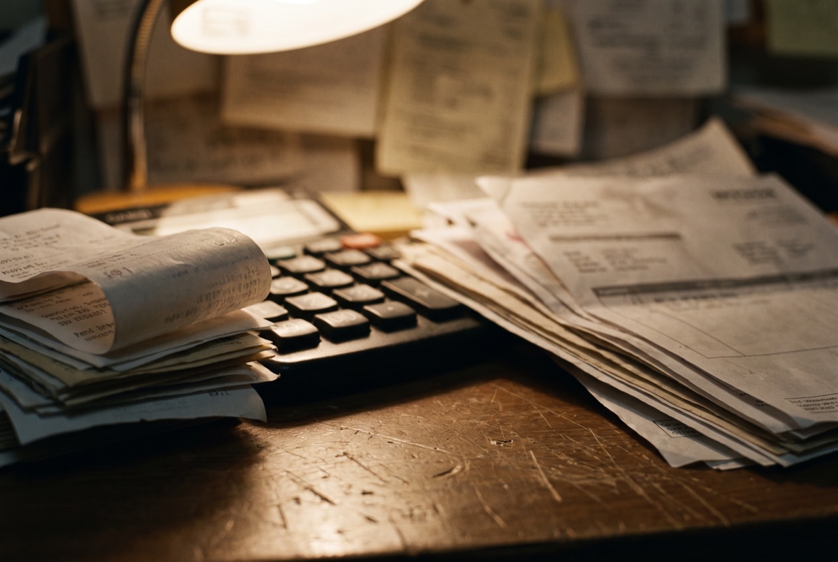 A stack of receipts and invoices beside a calculator