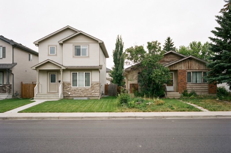 A modest new-construction home beside an older established resale home on the same street