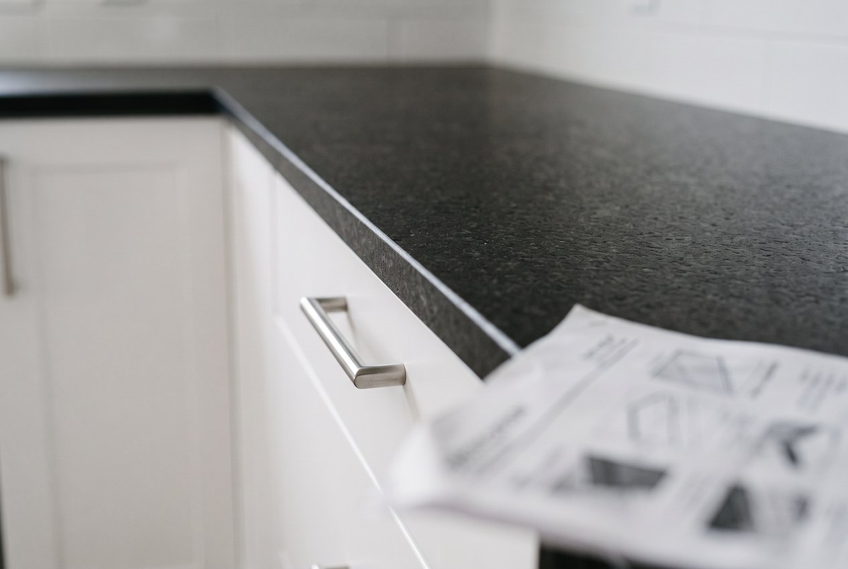 A specification sheet held up against an upgraded kitchen countertop and cabinetry in a show home