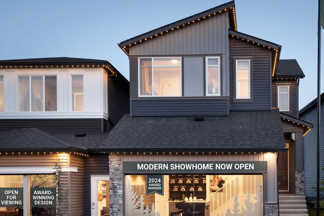 Dusk exterior of a new-construction show home in Edmonton with string lights and a lit garage-level display